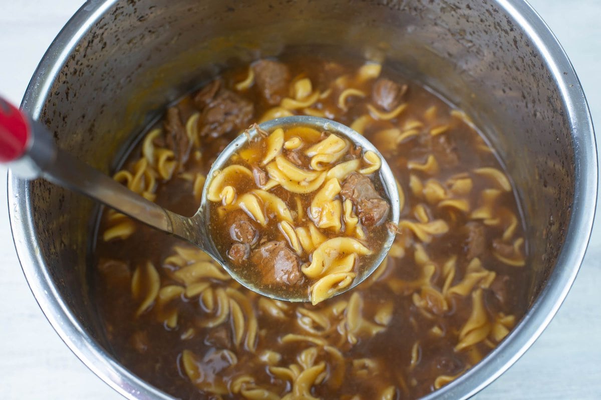 A ladle full of beef, egg noodle and a thick gravy.