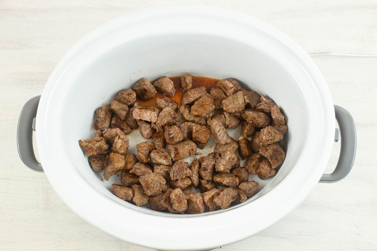 Browned stew meat in the bottom of a crock pot.