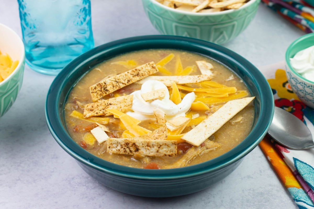 Cheesy Enchilada Soup bowl topped with cheese, sour cream and chips.