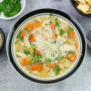 Chicken Pastina Soup in a bowl garnished with parsley and Parmesan cheese.