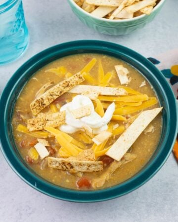 A bowl filled with Chicken Enchilada Soup garnished with sour cream, cheese and toasted tortilla chips.