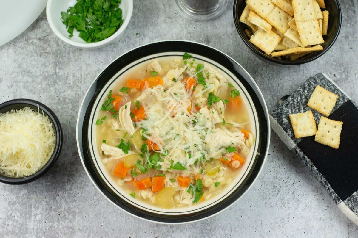 A boel of Chicken Pastina Soup served with a bowl on mini saltine crackers.