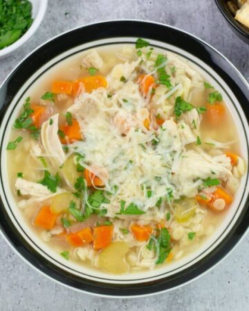 Chicken Pastina Soup in a bowl garnished with parsley and Parmesan cheese.