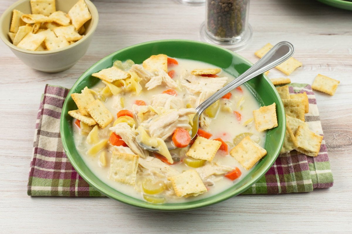 A bowl of creamy chicken noodle soup served with crackers.