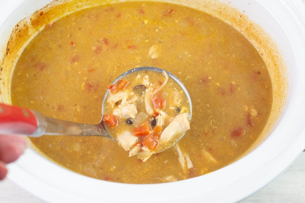 A ladle full of Chicken Enchilada Soup over the crock pot before serving in a bowl.