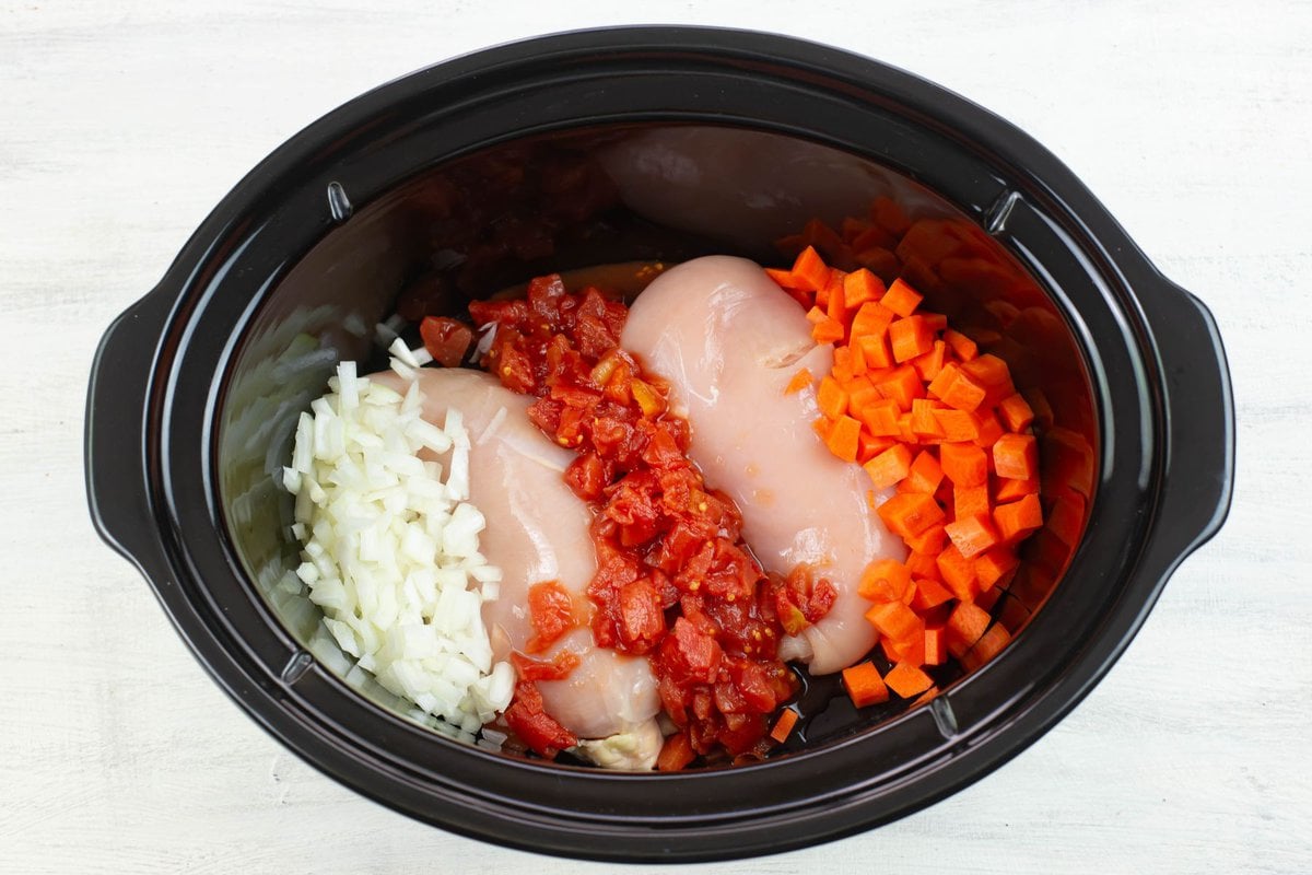 Boneless chicken, diced onion, diced tomatoes and carrots for soup in a crock pot.