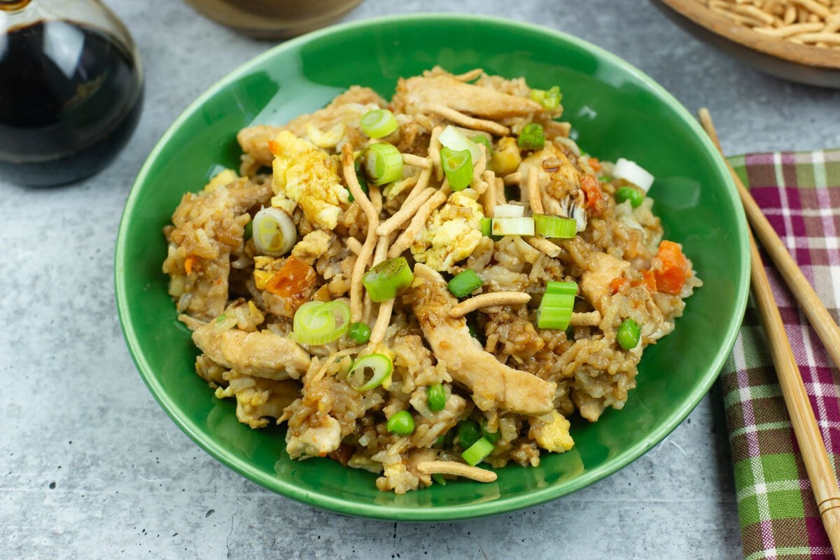 Topping a serving of chicken fried rice with sliced green onions and crunchy chow mien noodles.