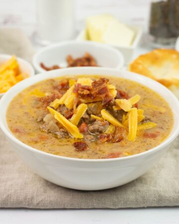 A bowl of Crock Pot Cheeseburger Soup topped with crumbled bacon and shredded cheese.