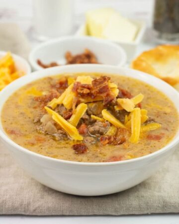 A bowl of Crock Pot Cheeseburger Soup topped with crumbled bacon and shredded cheese.