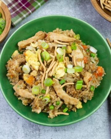 Chicken Fried Rice garnished with green onions and Chow mien noodles in a green bowl with chop sticks.