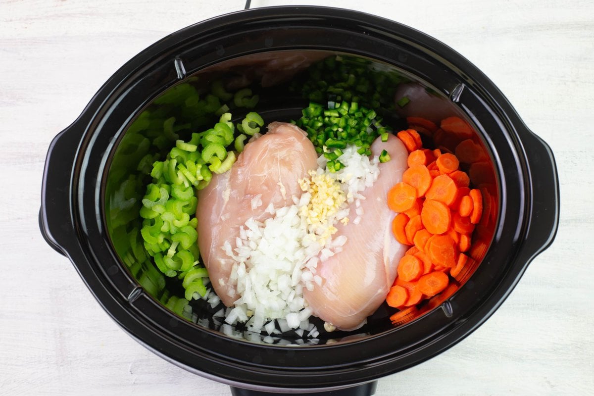Fresh vegetables arranged around the chicken in the crock pot.