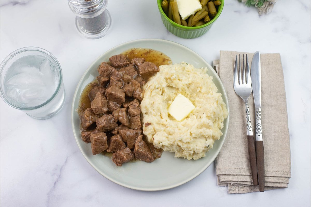 Beef tips served on a dinner plate with mashed potatoes and gravy.