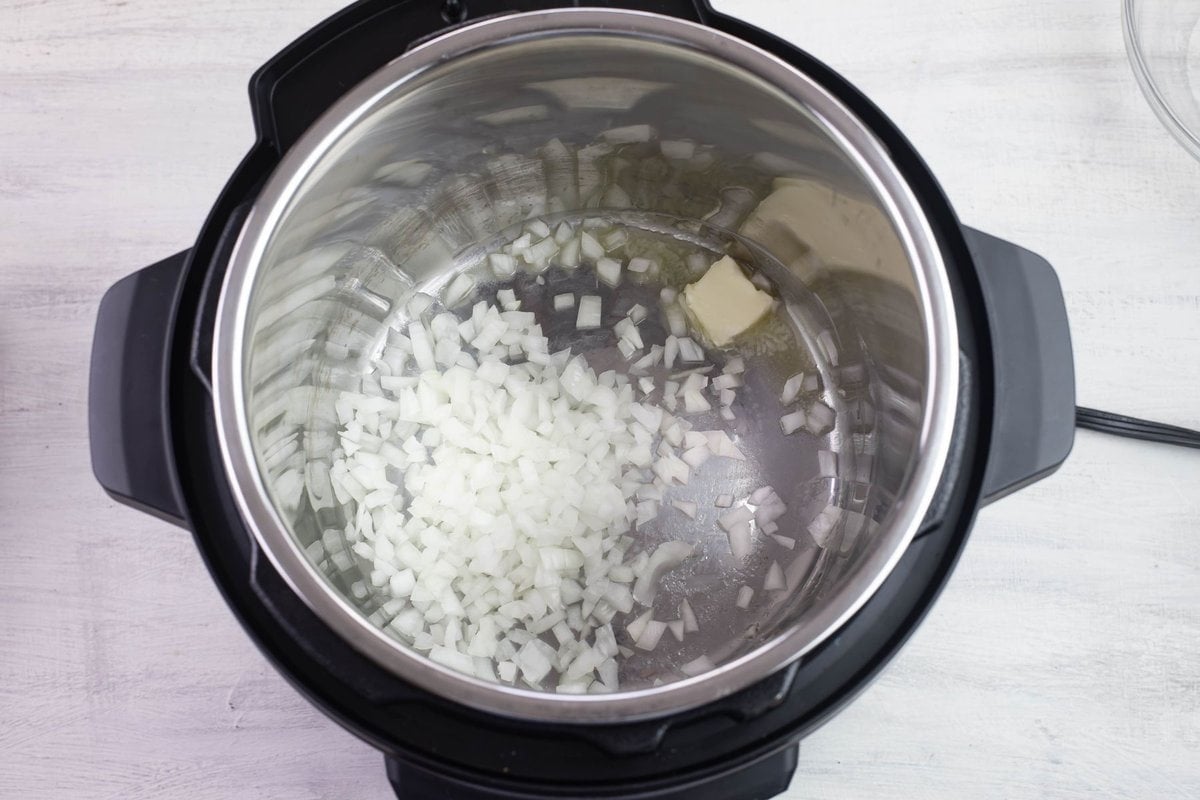 Diced onions and melting butter in the inner pot of the pressure cooker as sauteeing begins.