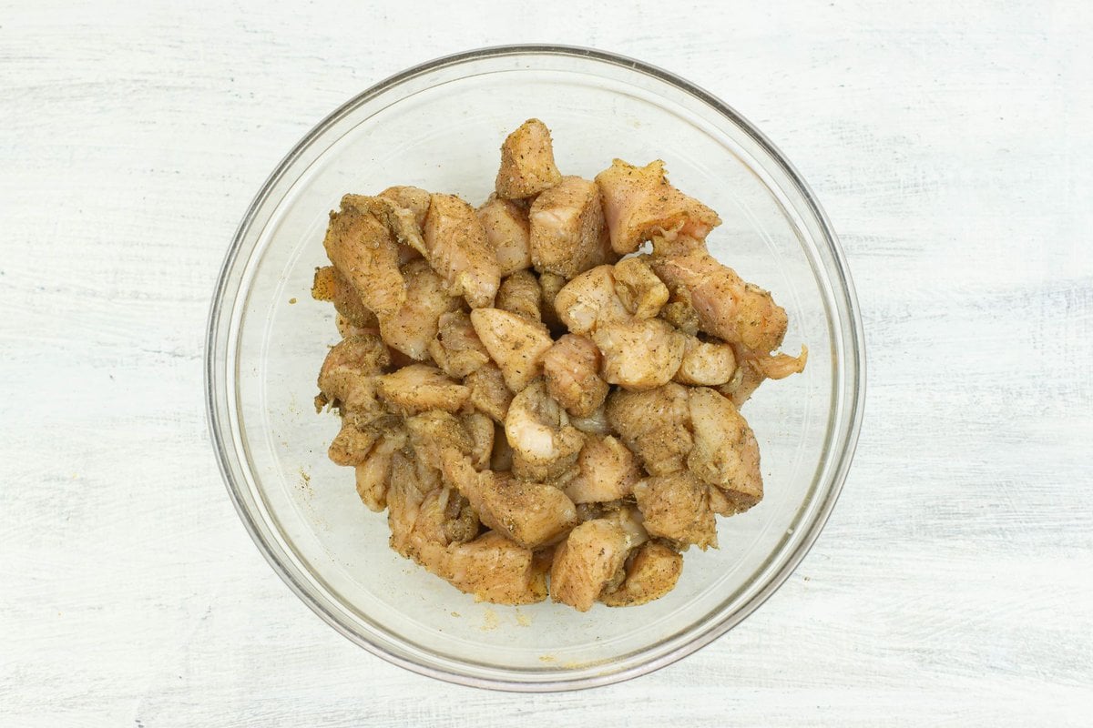 Cubed pieces of chicken covered in poultry seasoning in a bowl.