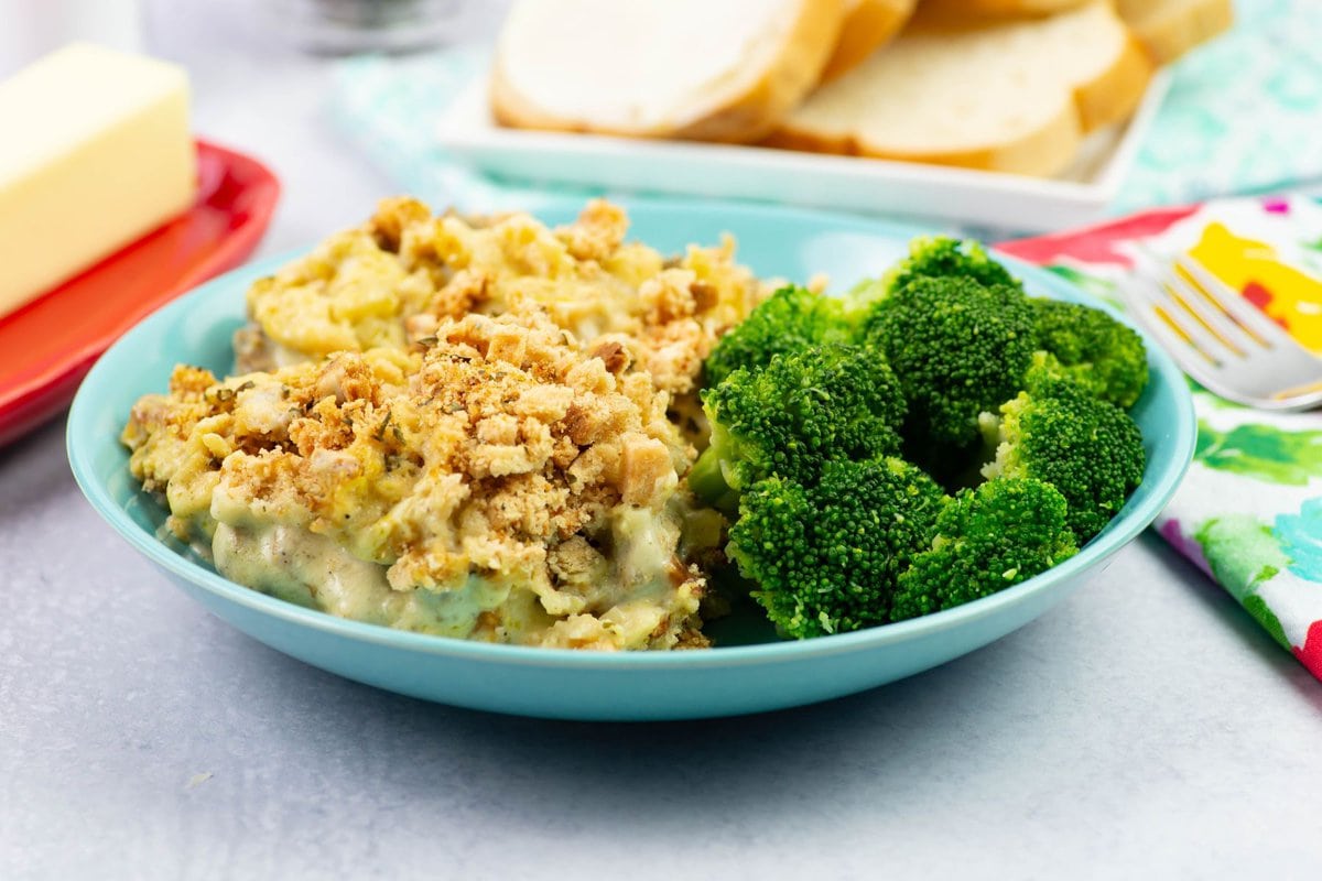 A serving of chicken and stuffing in a bowl with sliced bread and butter on a table.