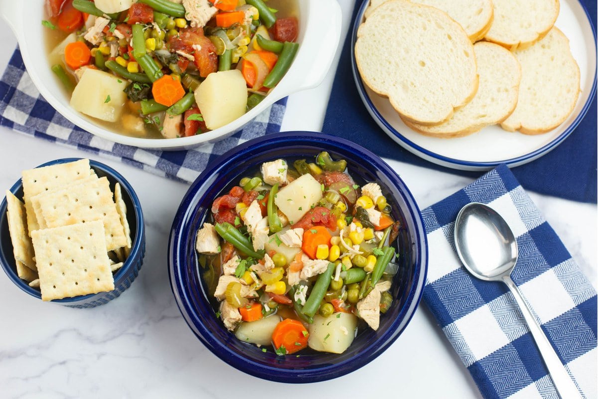 A serving of Slow Cooker Chicken and Veggie soup with crackers and bread.