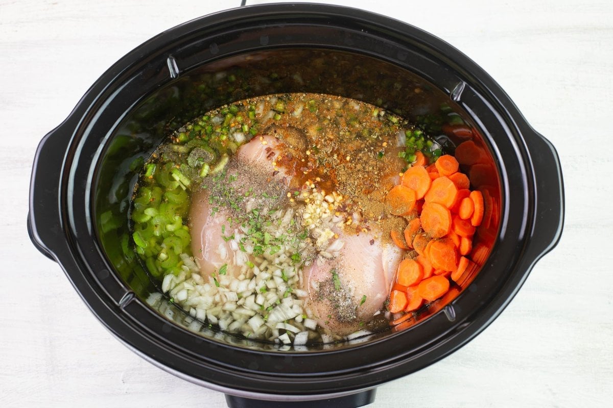 Chicken broth poured over the chicken, vegetables and seasoning in a slow cooker.