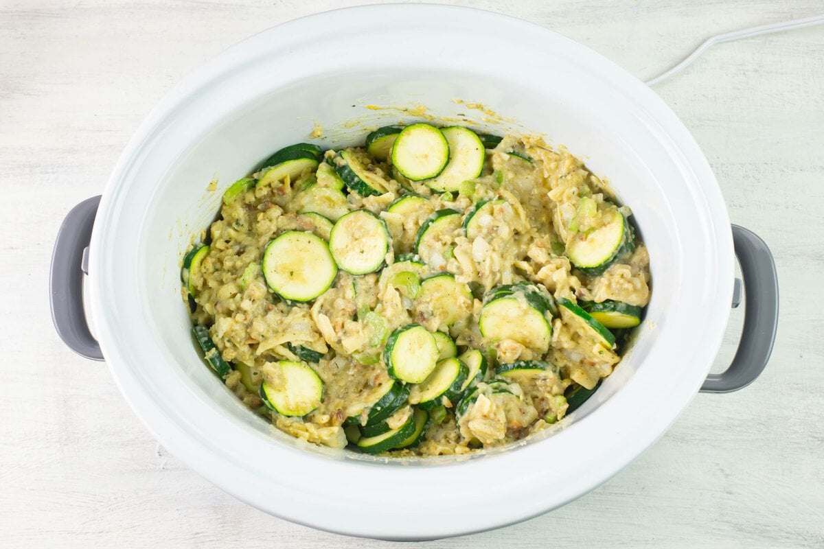 Sliced zucchini in a crock pot covered with casserole sauce ingredients.