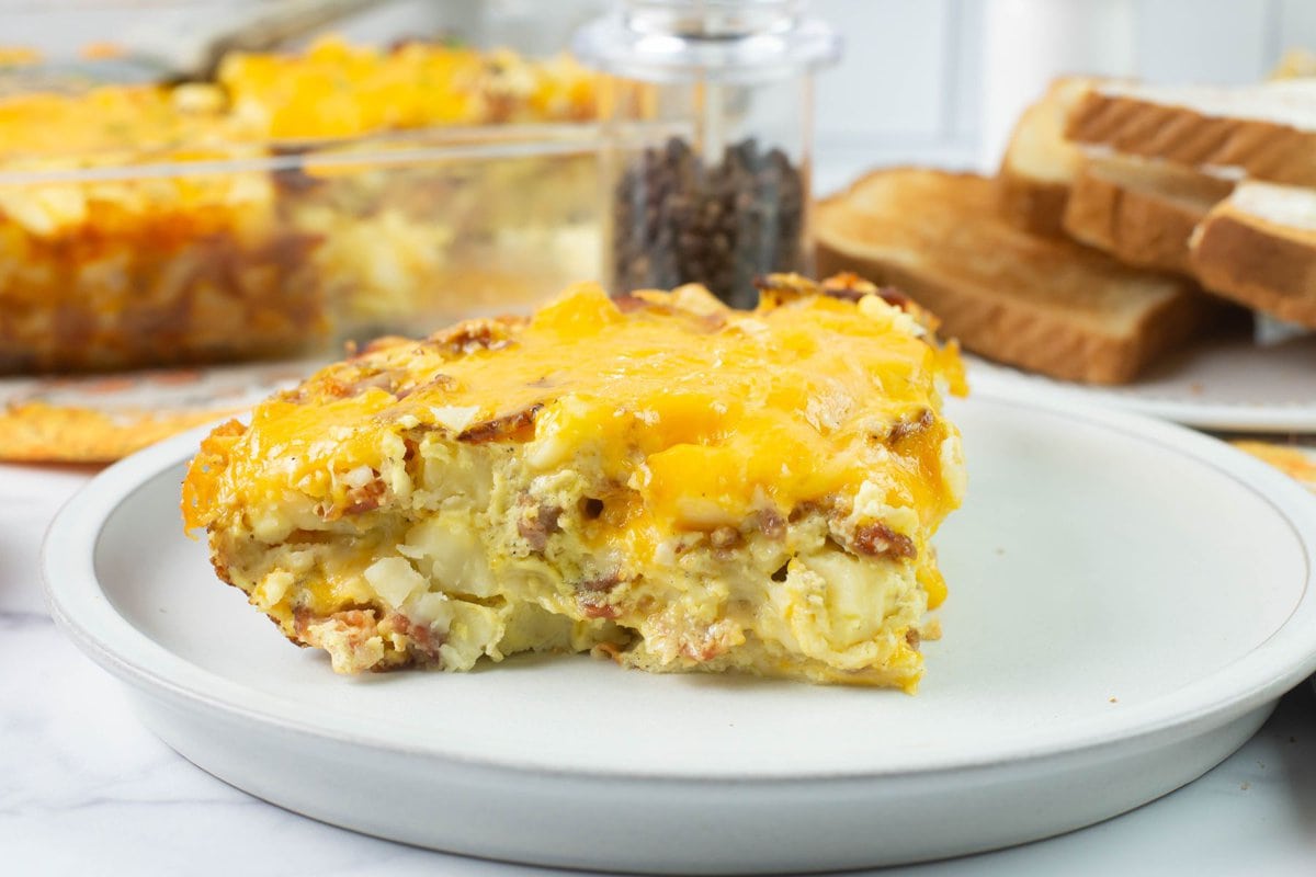A slice of egg, bacon, sausage, and cheese casserole with toast.