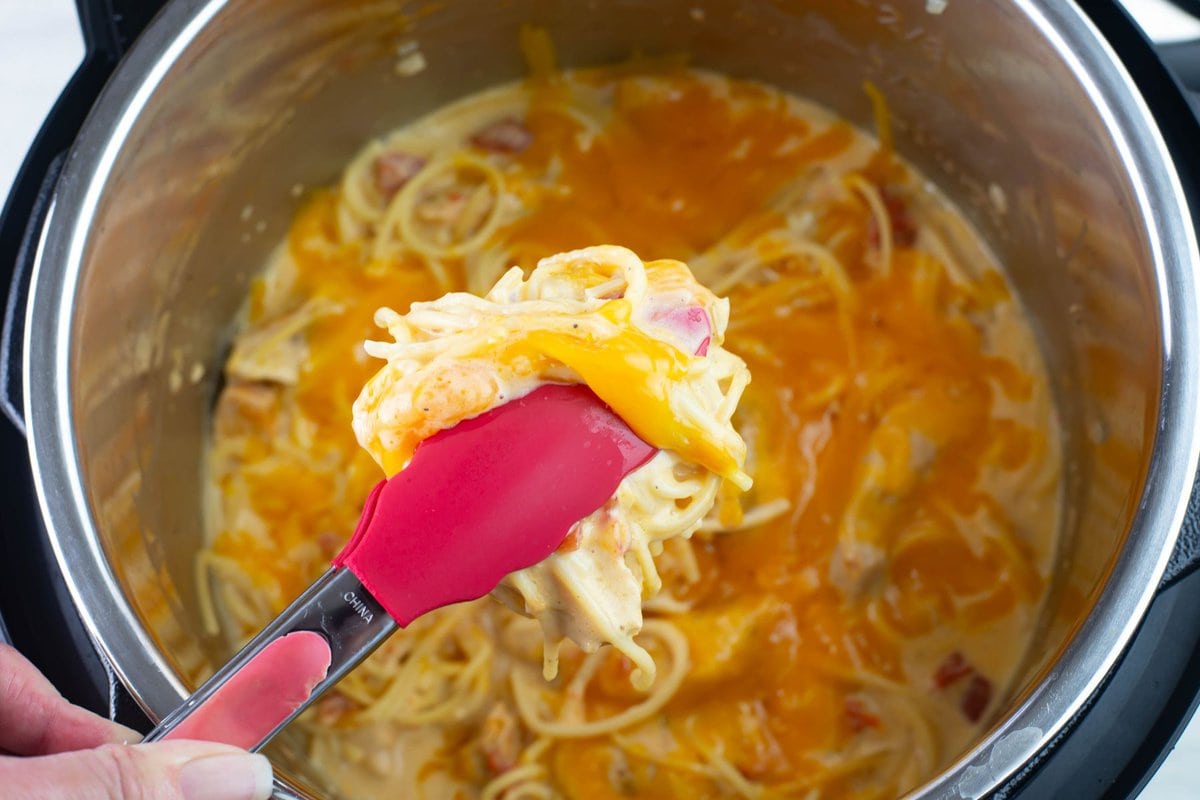 Lifting a serving of chicken with tongs from the Instant Pot.