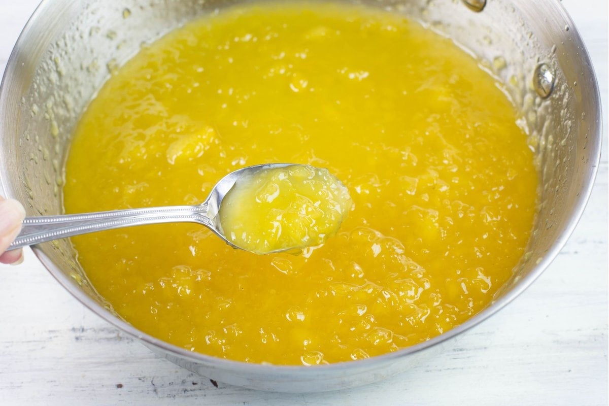 A spoon in a bowl of thickened homemade pineapple glaze.