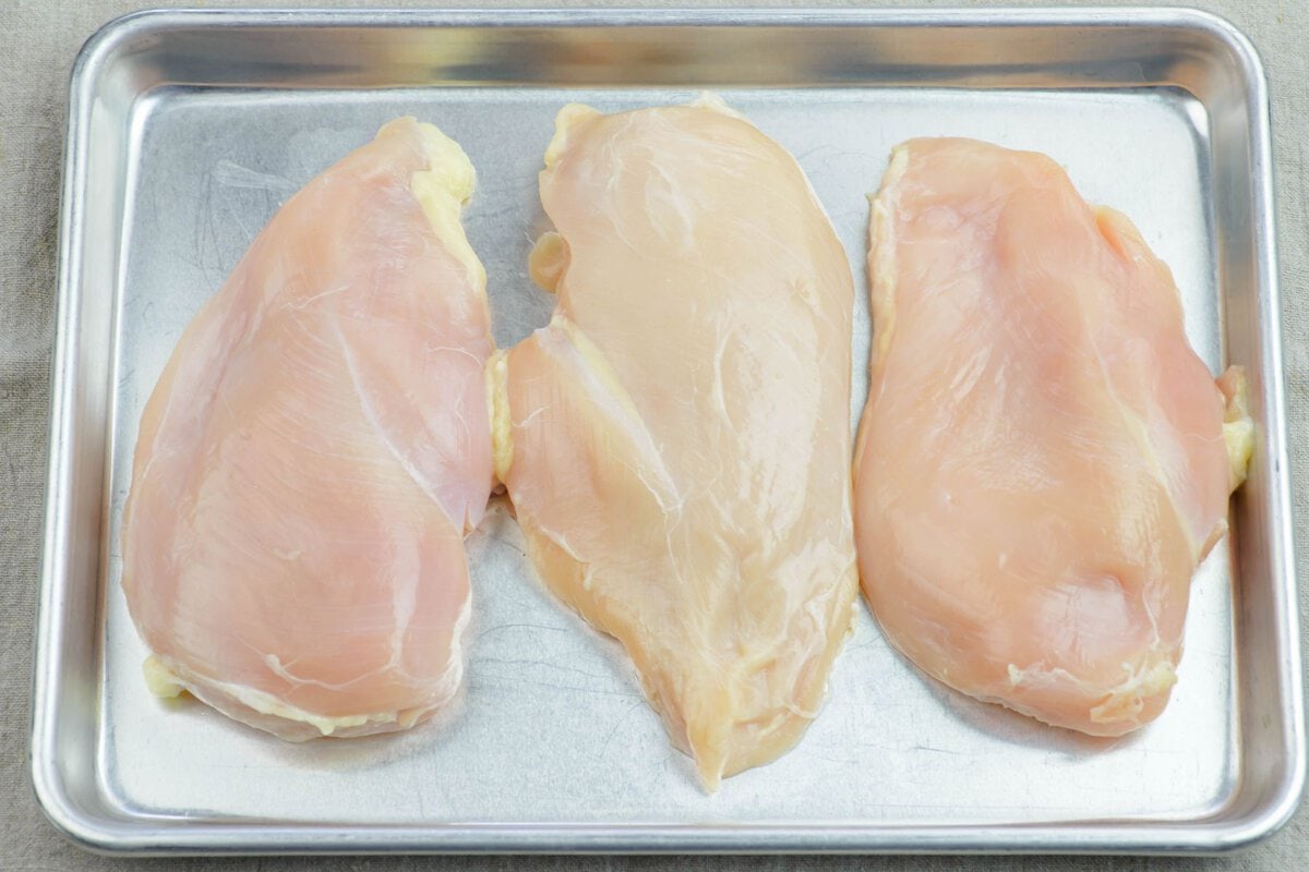 Three boneless chicken breast pieces on a metal tray.
