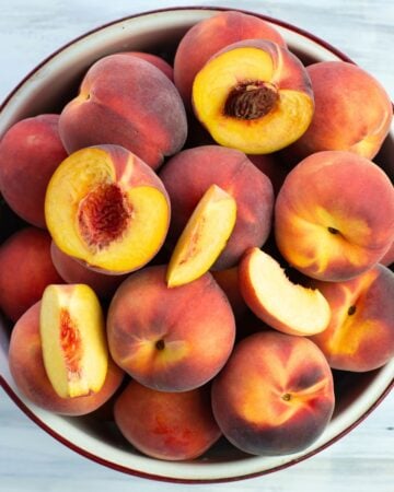 Sliced and whole fresh peaches in a metal colander.