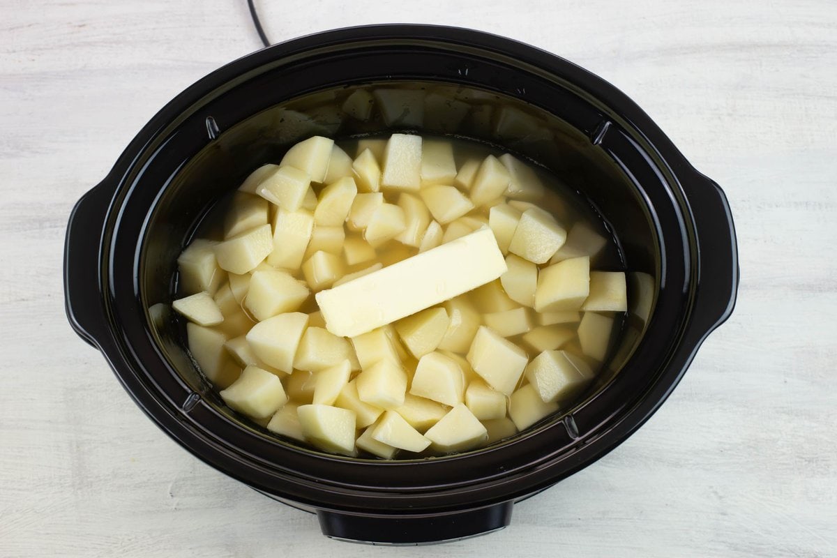 Adding the potatoes, chicken broth and butter in the slow cooker.