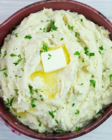 Serving bowl filled with Million Dollar Mashed Potatoes garnished with parsley.