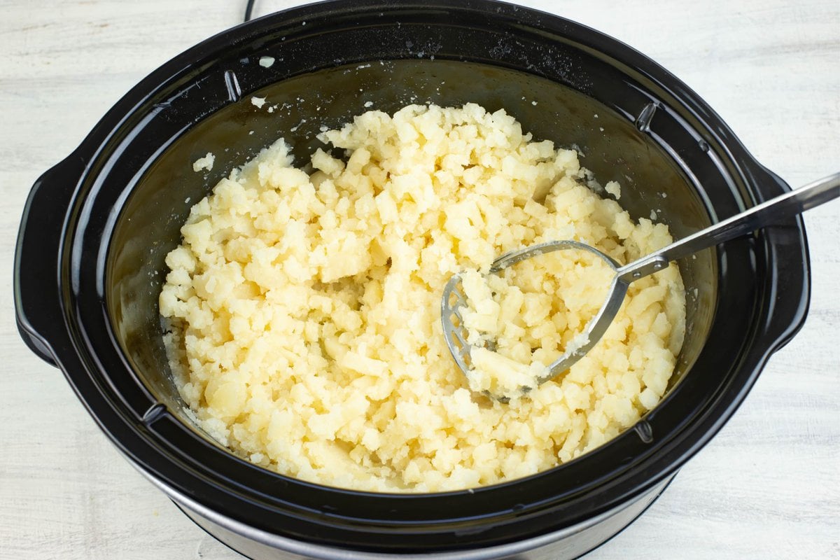 Mashing cooked potatoes in a warm slow cooker.