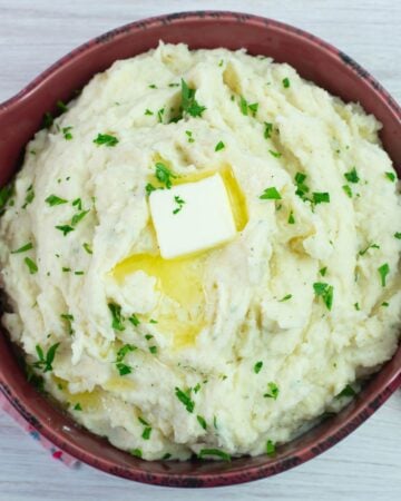 Serving bowl filled with Million Dollar Mashed Potatoes garnished with parsley.