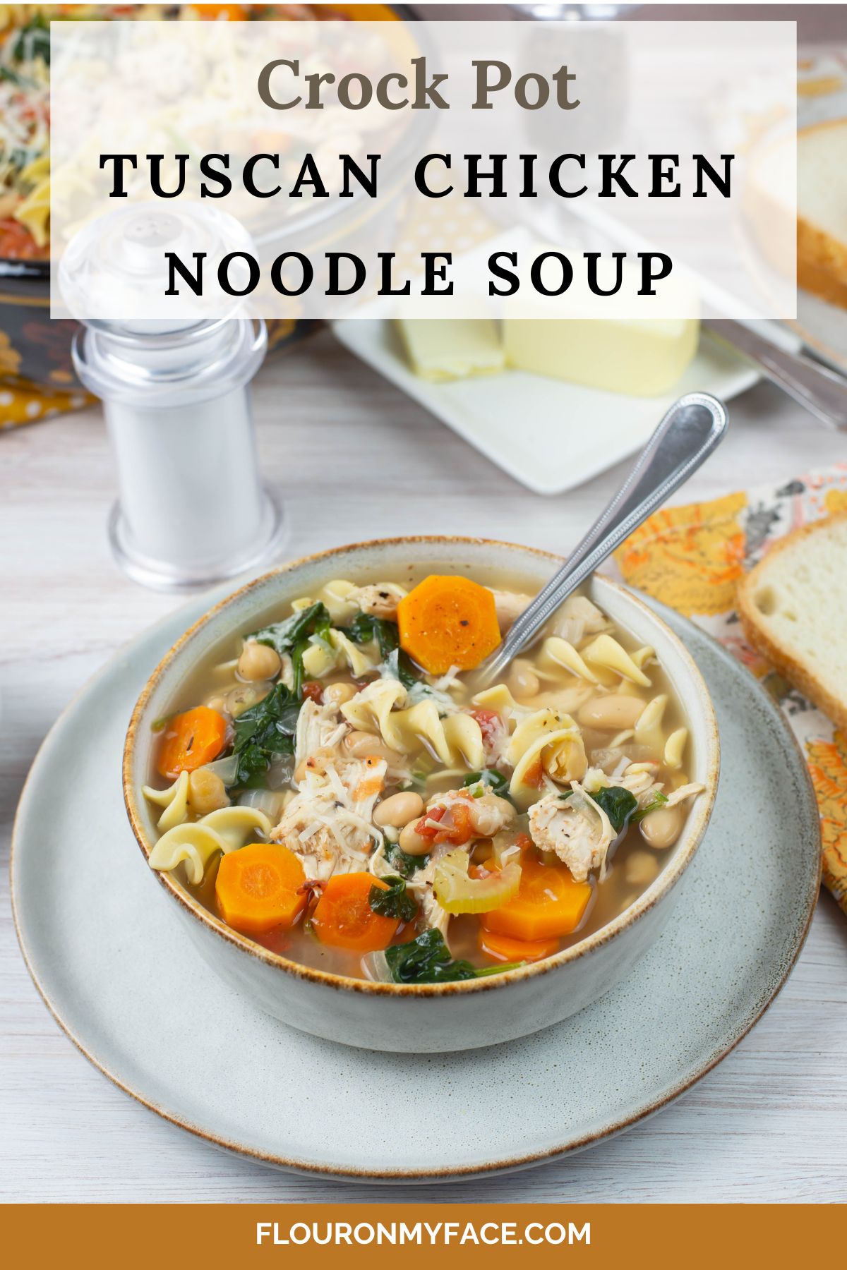 Tall vertical image of a bowl of Tuscan chicken noodle soup on a table with sliced bread in the background.