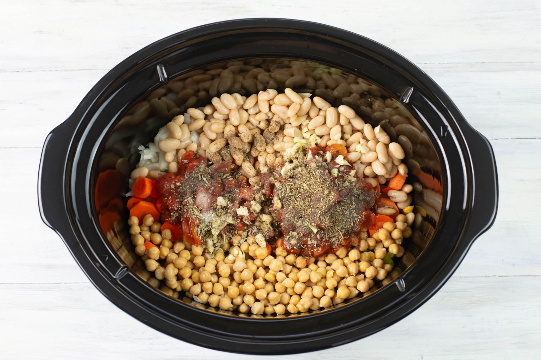 Beans, tomato, and seasonings for the soup added to the slow cooker.