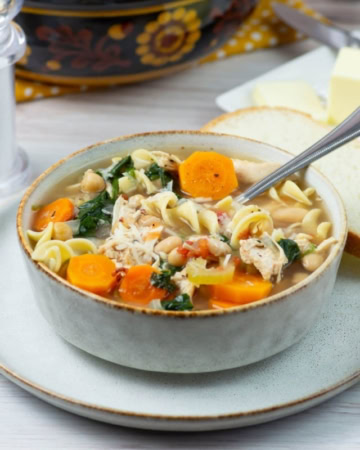 Tuscan Chicken Noodle Soup in a bowl with sliced bread in the background.