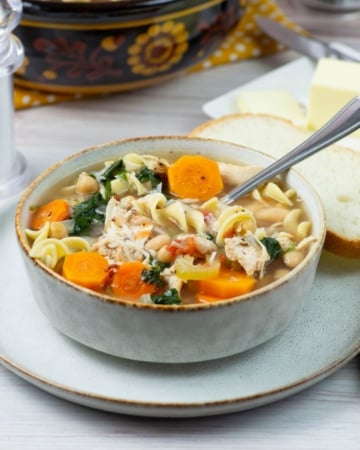 Tuscan Chicken Noodle Soup in a bowl with sliced bread in the background.