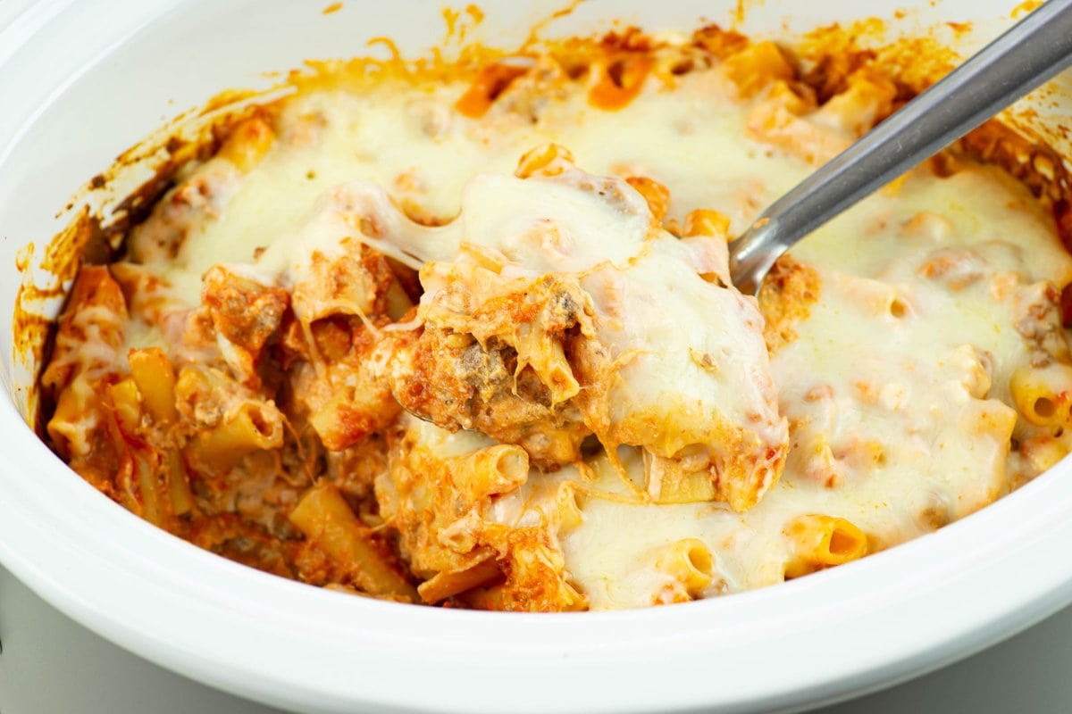 Scooping a serving of cheesy baked ziti out of a slow cooker.