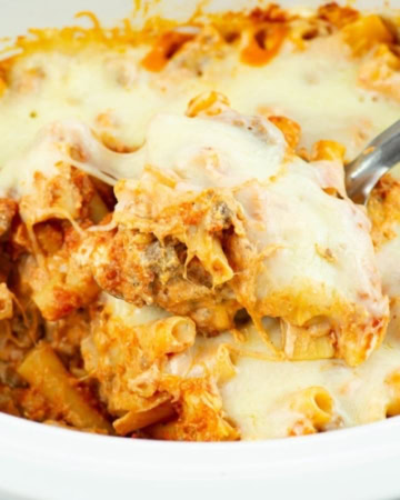 Scooping a serving of cheesy baked ziti out of a slow cooker.