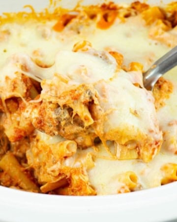 Scooping a serving of cheesy baked ziti out of a slow cooker.