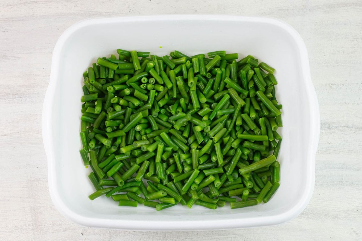 Bright vibrant green blanched green bean pieces in a large plastic tub.