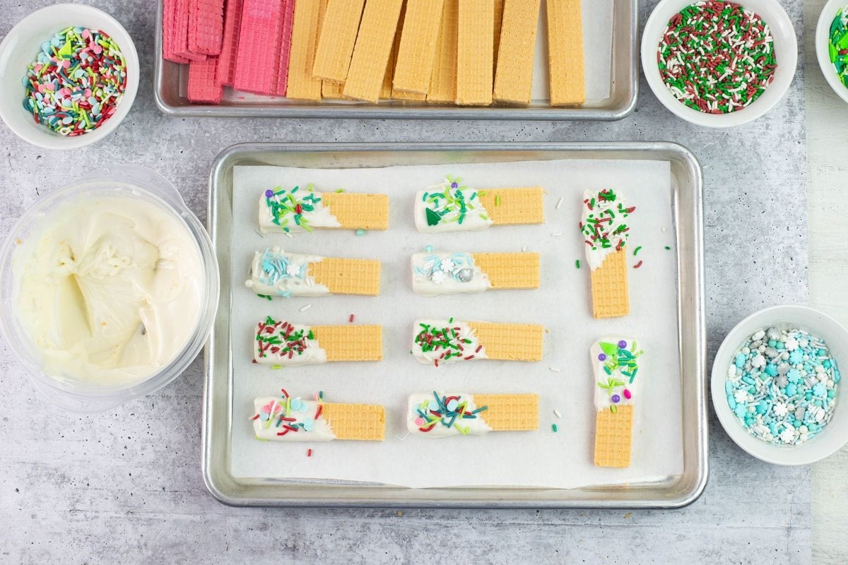 Vanilla wafer cookies decorated with white chocolate and sprinkles on a tray.