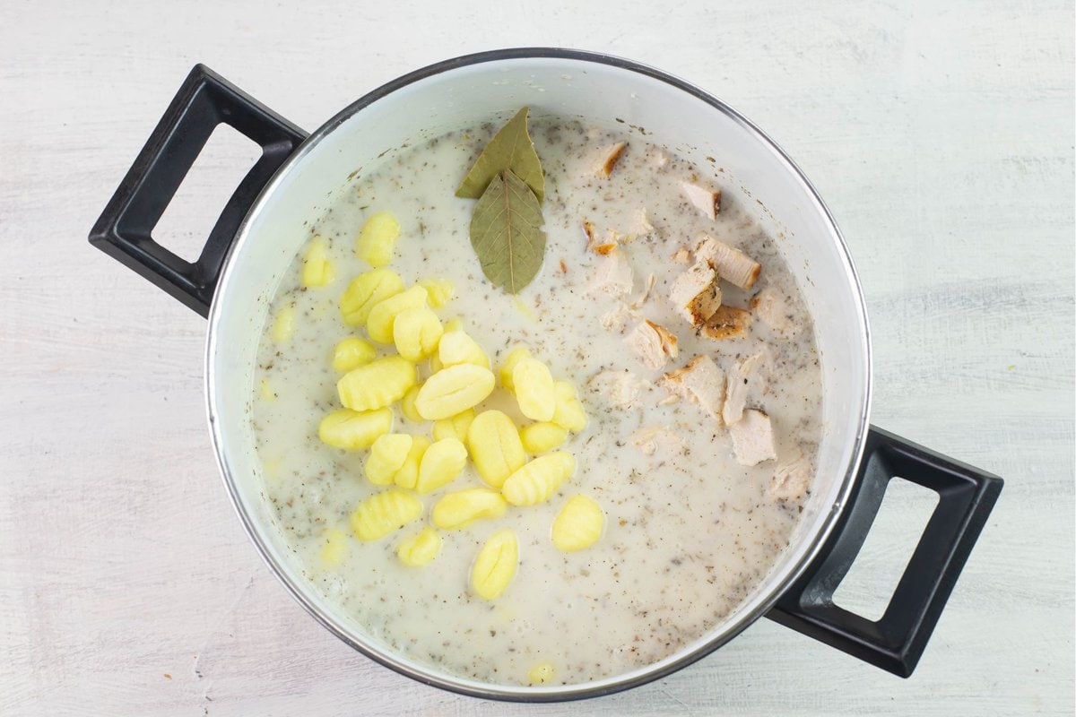 Adding potato Gnocchi, cooked chicken and dried bay leaves to the pot.