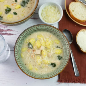 A bowl of alfredo gnocchi soup served with buttered bread.