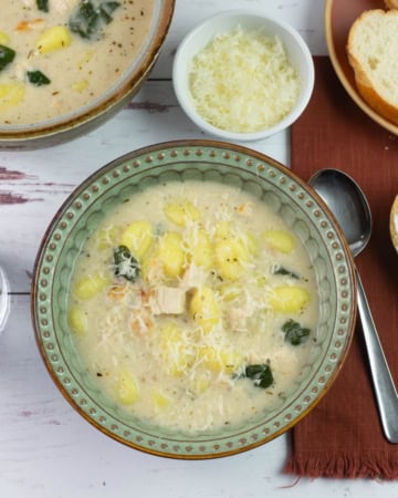 A bowl of alfredo gnocchi soup served with buttered bread.