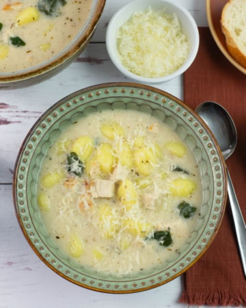 A bowl of alfredo gnocchi soup served with buttered bread.