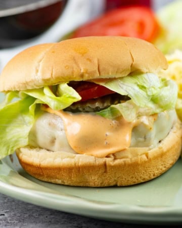 Chicken burger on a bun with toppings served on a plate with sides.