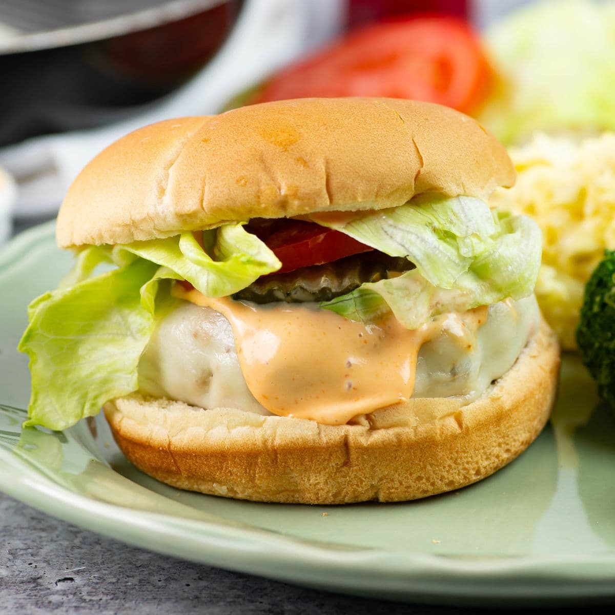 Chicken burger on a bun with toppings served on a plate with sides.