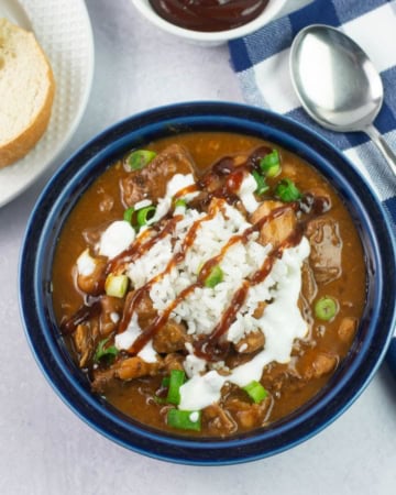 A bowl of pulled pork chili garnished with rice and bbq sauce.