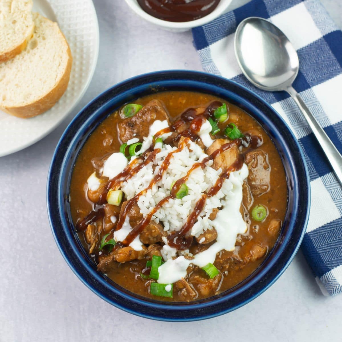 A bowl of pulled pork chili garnished with rice and bbq sauce.