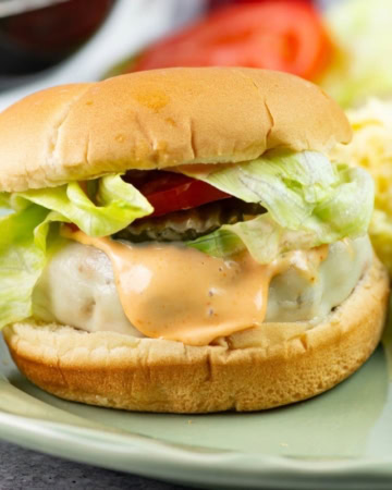 Chicken burger on a bun with toppings served on a plate with sides.