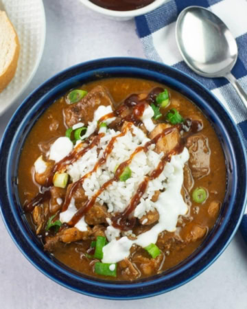 A bowl of pulled pork chili garnished with rice and bbq sauce.